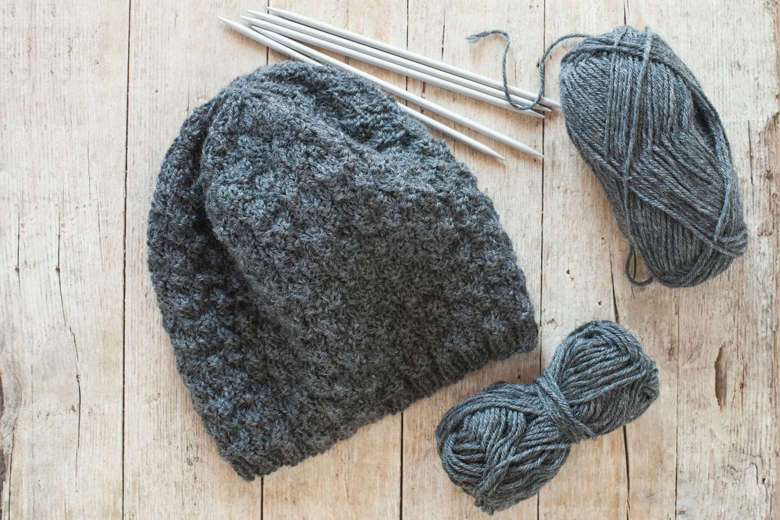 A handmade hat and two skeins of yarn on a wooden table