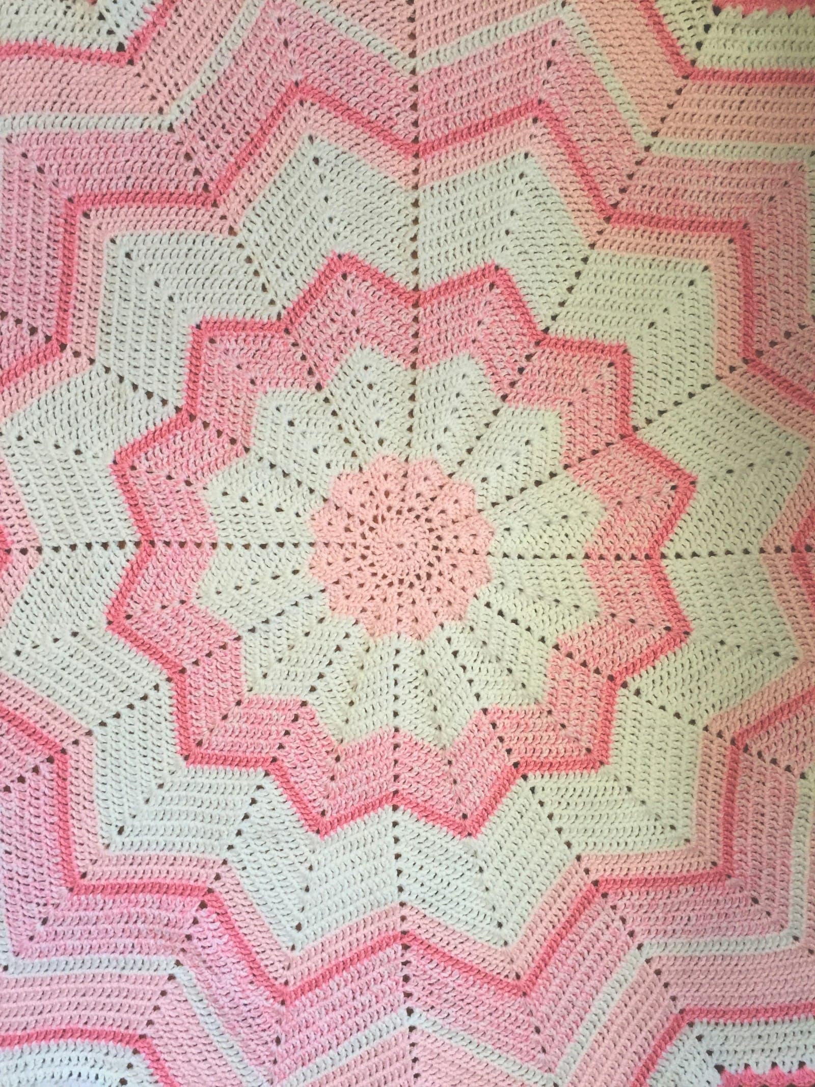 A pink and cream star-patterned crocheted baby blanket, worked in a ripple design
