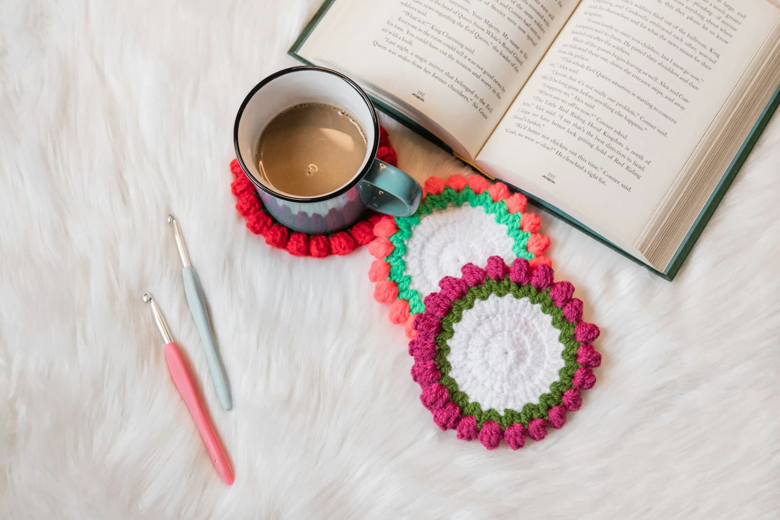 Two round crocheted coasters with bright bobble-stitch borders, next to a mug of coffee and an open book