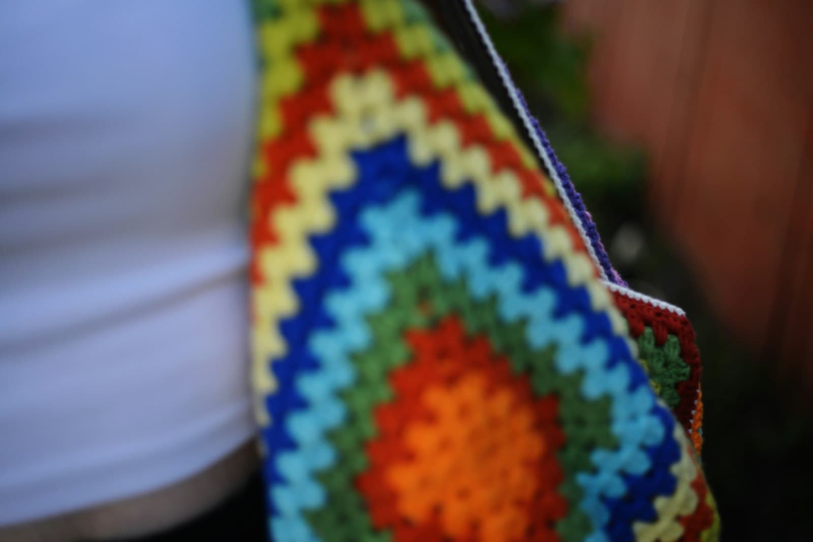 A colorful granny-square style crocheted bag with bold striped patterning, carried over a shoulder