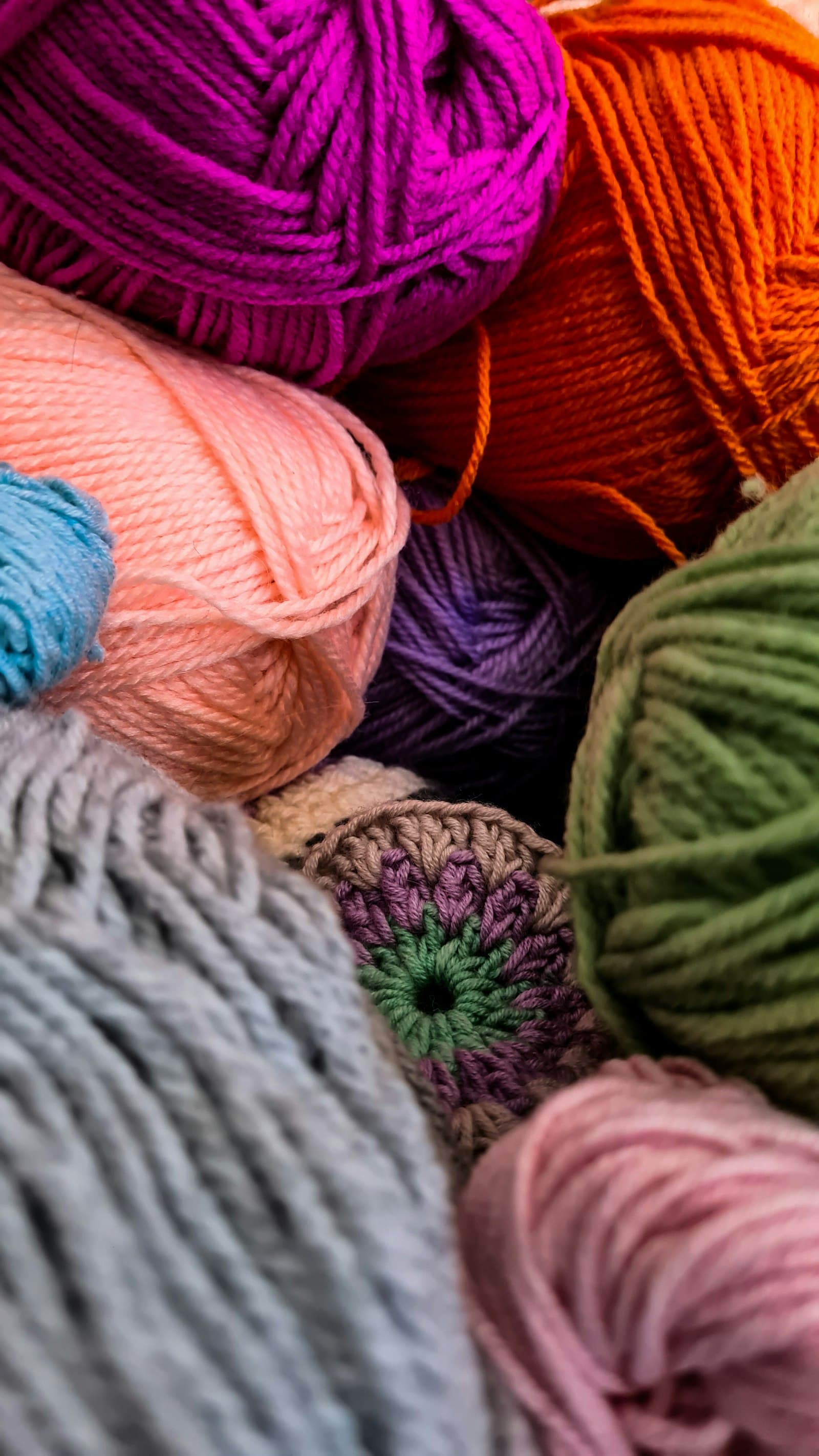 A pile of colorful crocheted yarn balls in pink, orange, purple, and green, scattered on a dark floral fabric