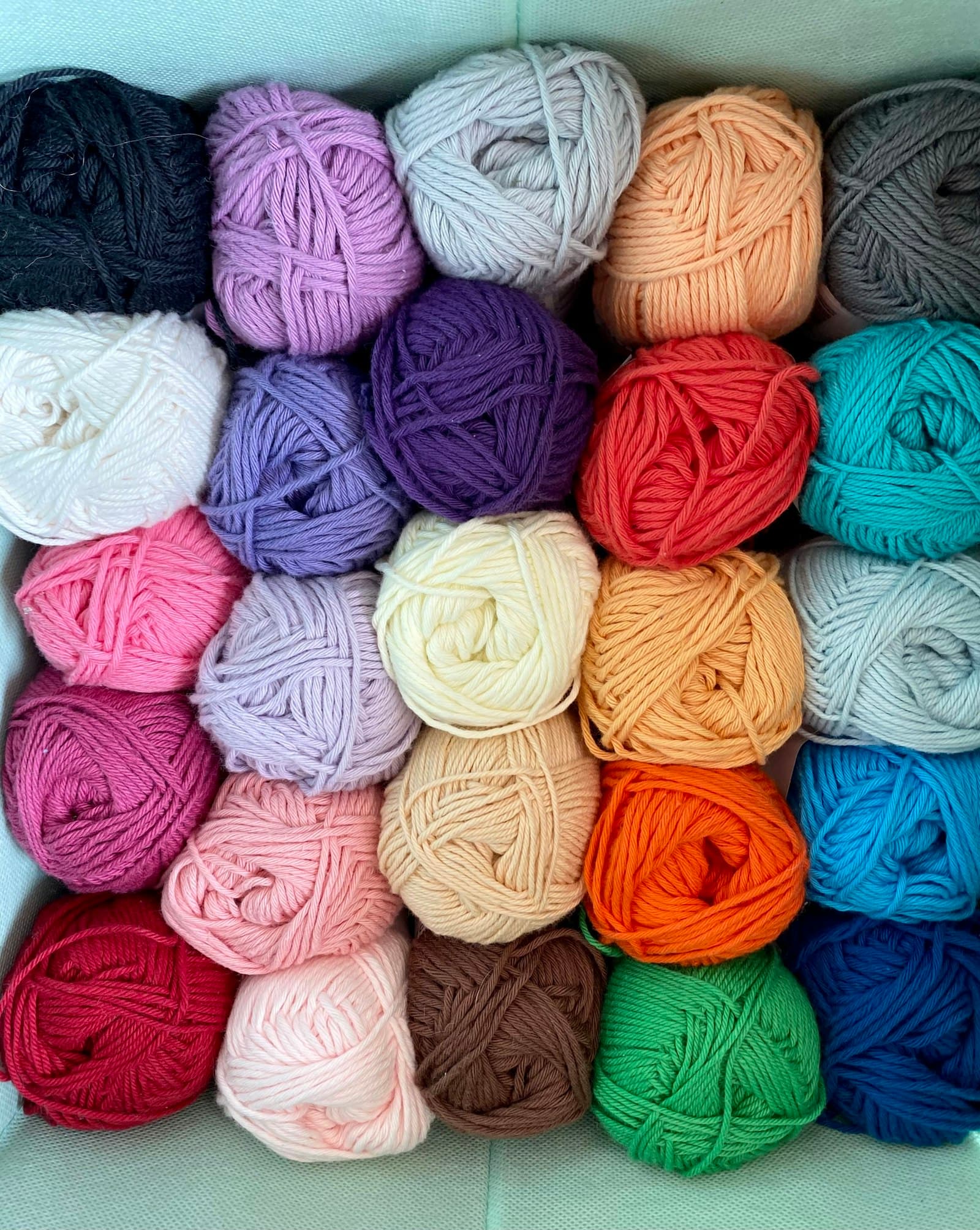 Rows of colorful yarn balls in pink, purple, cream, orange, and blue, arranged closely together