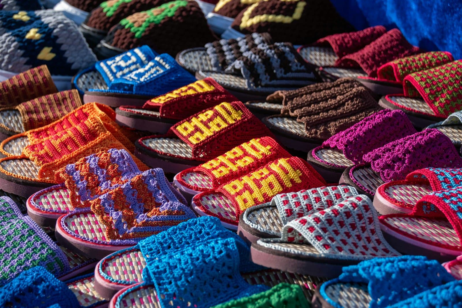 A colorful market display of handmade crochet slide sandals in many bold patterns and colors