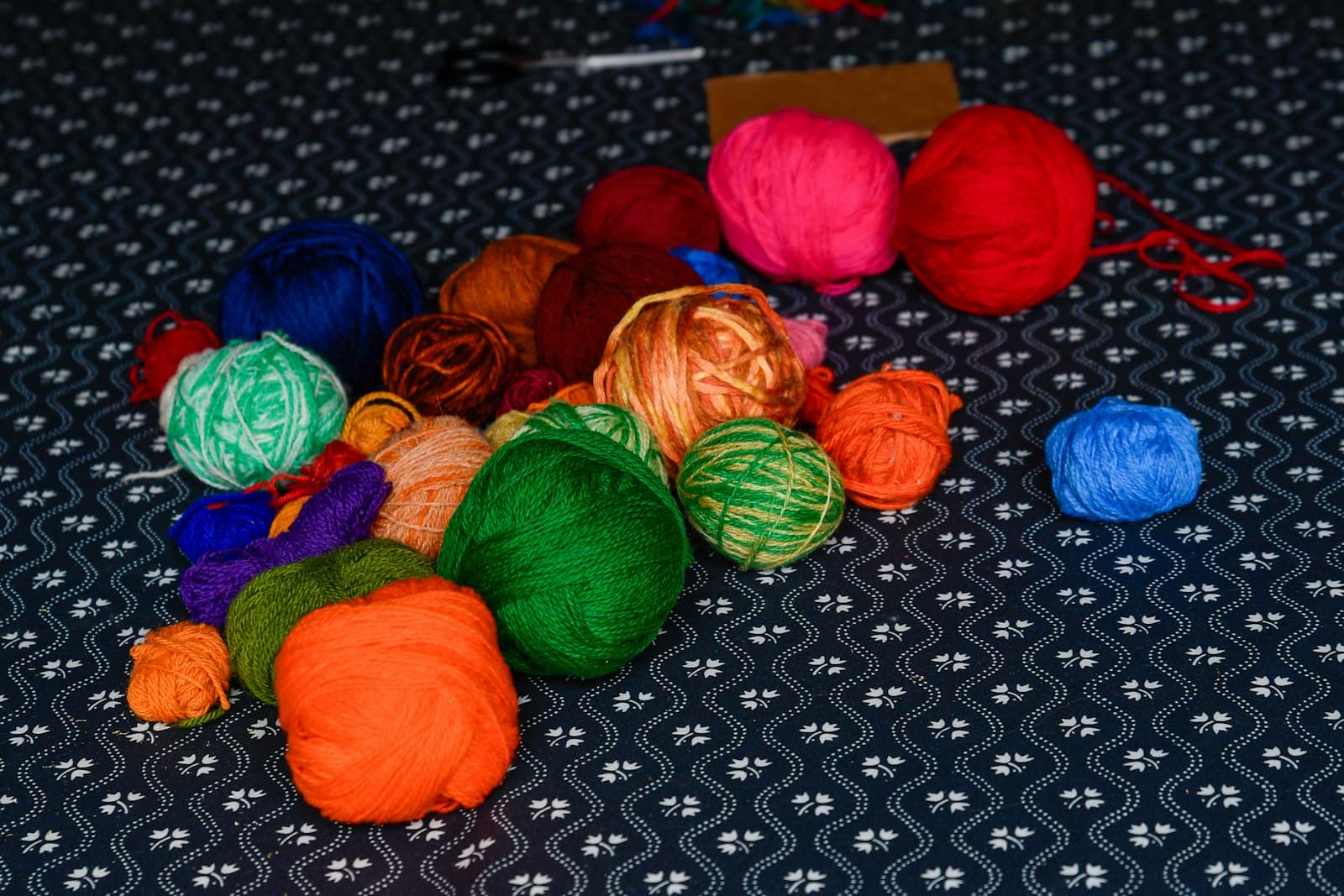 A neat row of colorful yarn balls in blue, pink, orange, and green, arranged on a dark patterned tablecloth