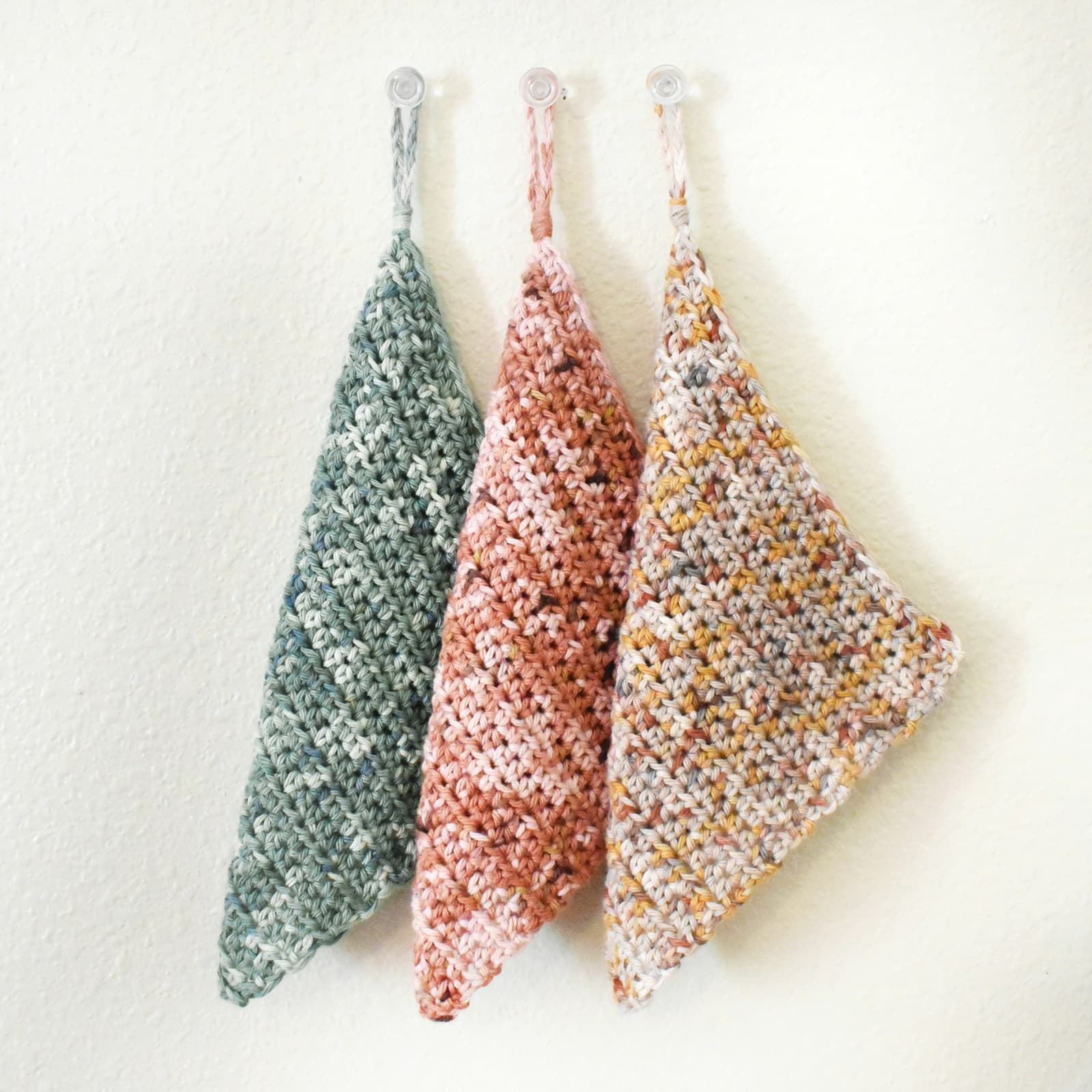 Three crocheted washcloths hanging from wooden hooks