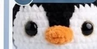 Close-up of the finished penguin face, showing the black and white color-blocked head with round safety eyes and the orange beak centered between them