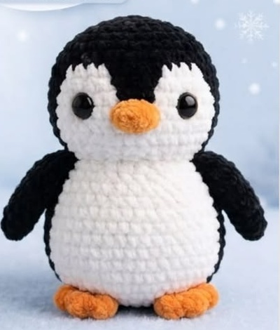 Finished crocheted plush penguin sitting upright, black and white body with an orange beak and feet