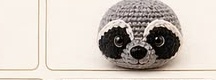 Finished grey crocheted raccoon head with black eye masks, pink-lined ears, cream muzzle, and embroidered nose already attached