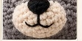 Close-up of the finished raccoon face showing the embroidered black triangle nose and smile centered on the cream muzzle